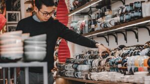 A man browsing a variety of ceramic mugs and bowls inside a shop in Hanoi, Vietnam.