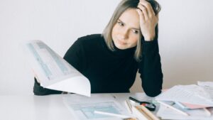 A stressed small business owner sitting at a cluttered desk reviewing invoices and financial paperwork in a back office