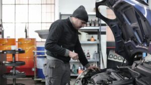 Mechanic working under the open bonnet of a car in an independent repair workshop