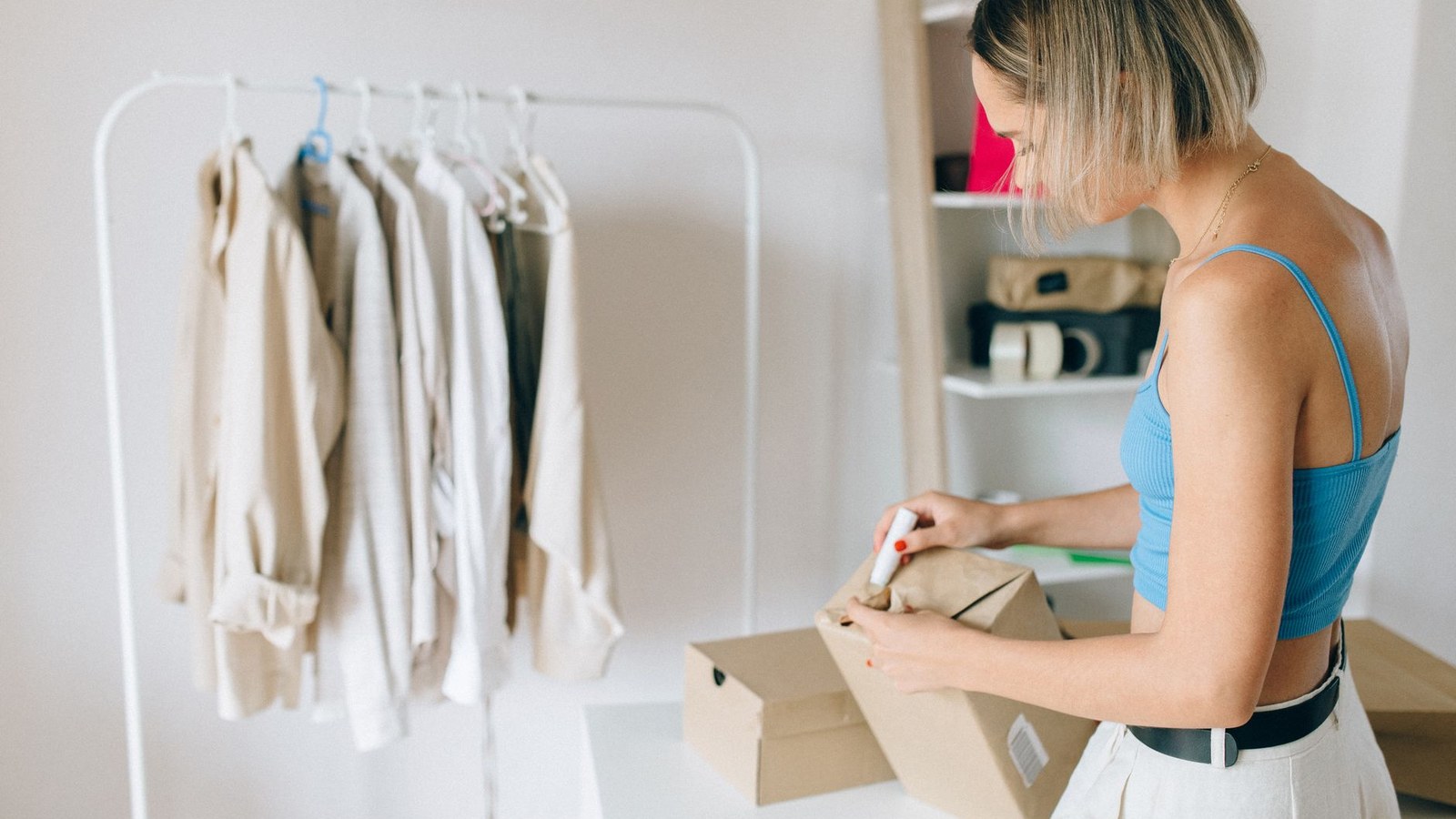 A retail worker packing clothing into boxes inside a nearly empty fashion store with bare racks in the background